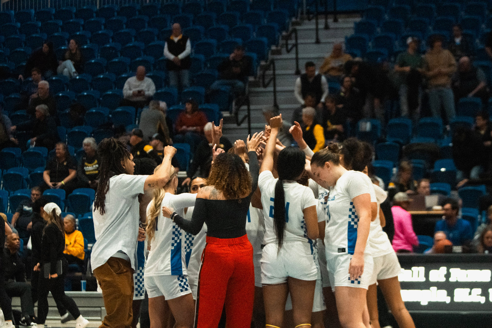 Women's basketball coaches and players huddling in a circle on the court