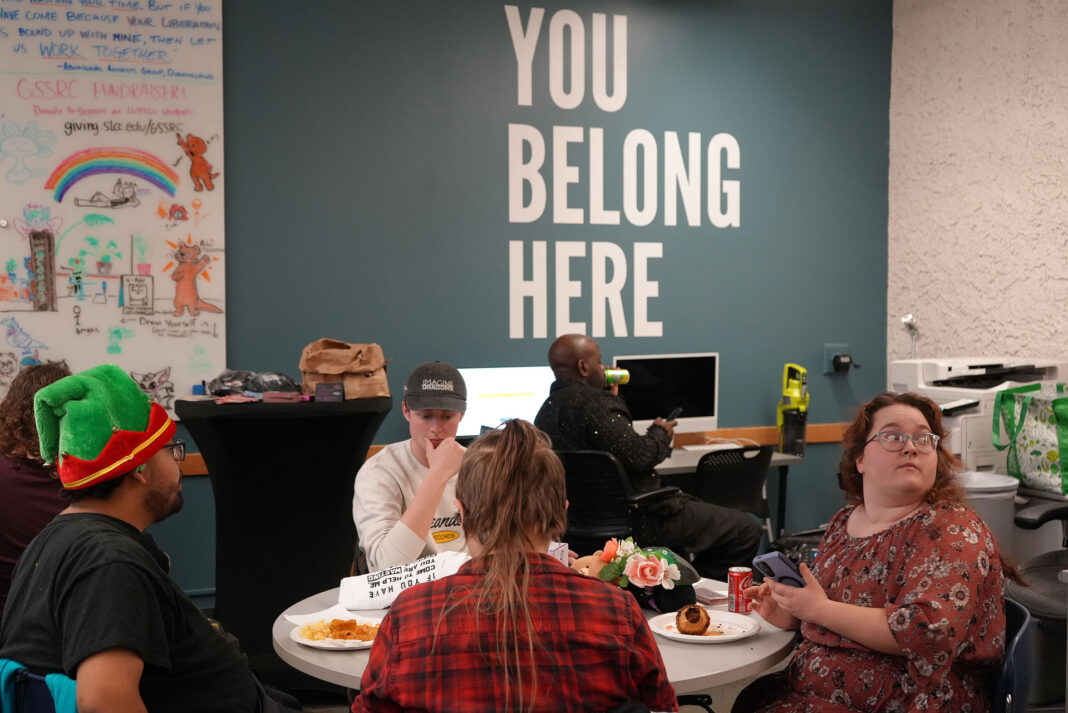 People socializing in a room with a wall that reads "You Belong Here"