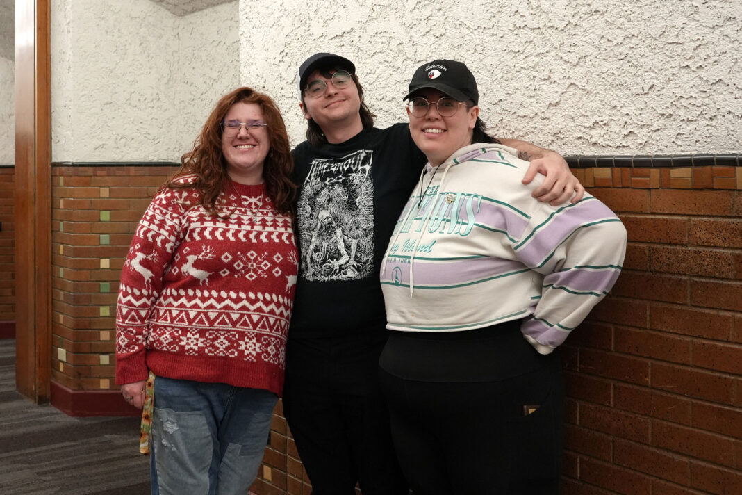 Three people standing together and smiling for a photo in a hallway