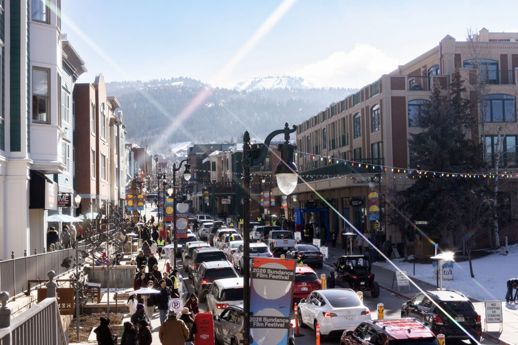 Landscape photo of a higher angle of Main Street with cars, people, buildings, and mountains in frame. Light streak on purpose