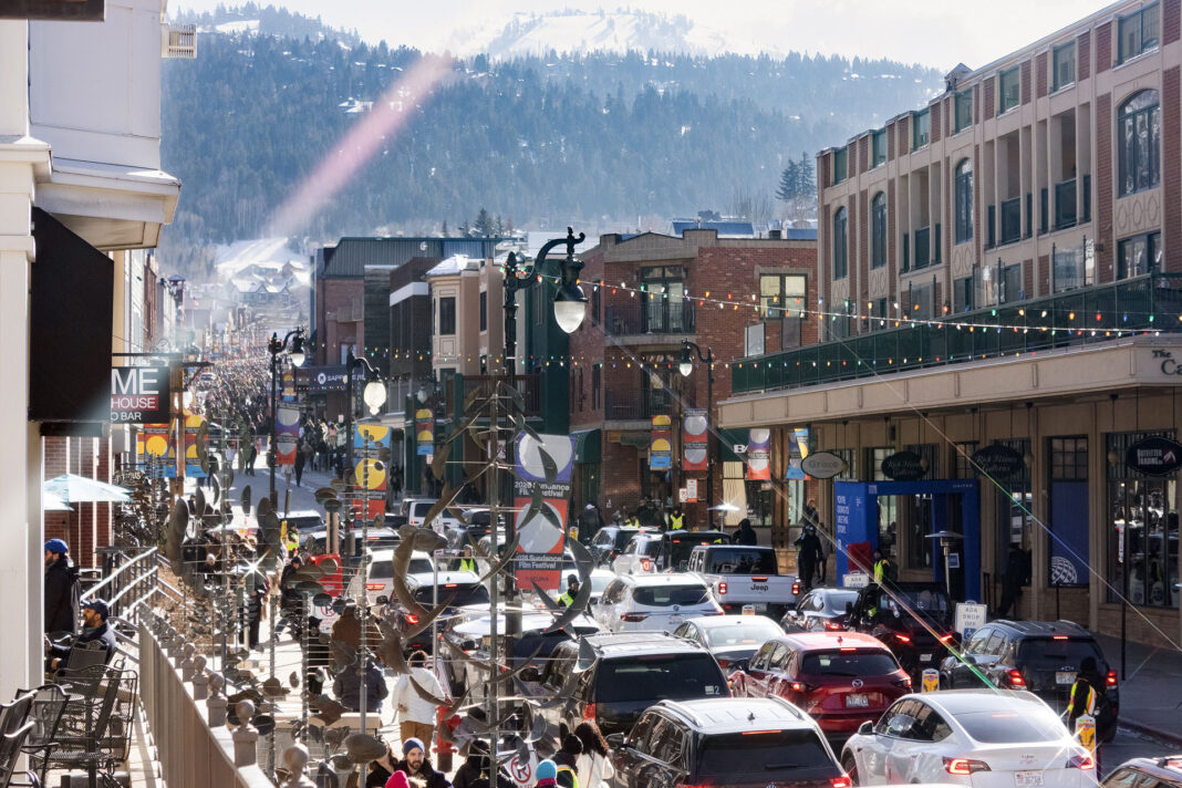 Landscape photo of traffic on Main Street with people crowding the sidewalk with public art in frame. Light streaks are on purpose