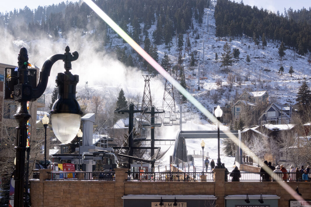 Landscape photo of a ski lift, bridge, people, and mountains with snowy clouds. Light streaks on purpose