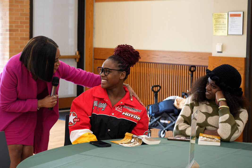 Deja speaking into a microphone next to Rita and another attendee
