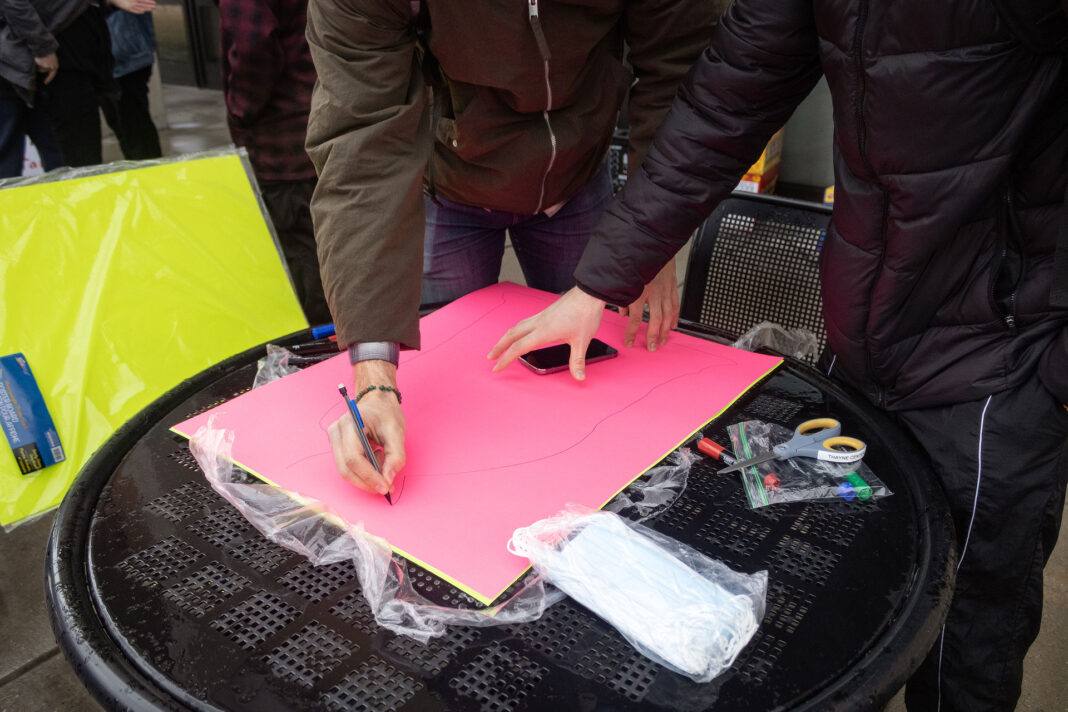 Landscape photo of two SLCC protesters drawing on a neon pink poster board