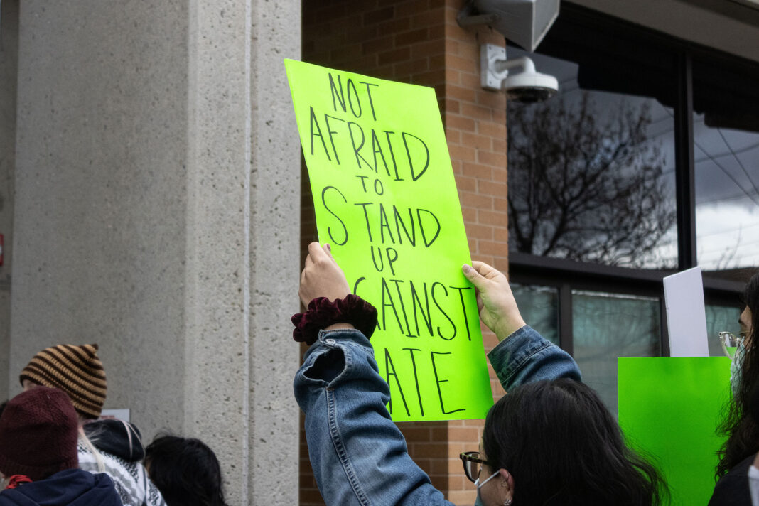 Landscape photo of a neon green sign being held above a SLCC protesters head