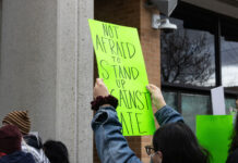 Opinion: SLCC students deserve better than DHS recruitment Landscape photo of a neon green sign being held above a SLCC protesters head