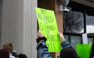 Opinion: SLCC students deserve better than DHS recruitment Landscape photo of a neon green sign being held above a SLCC protesters head