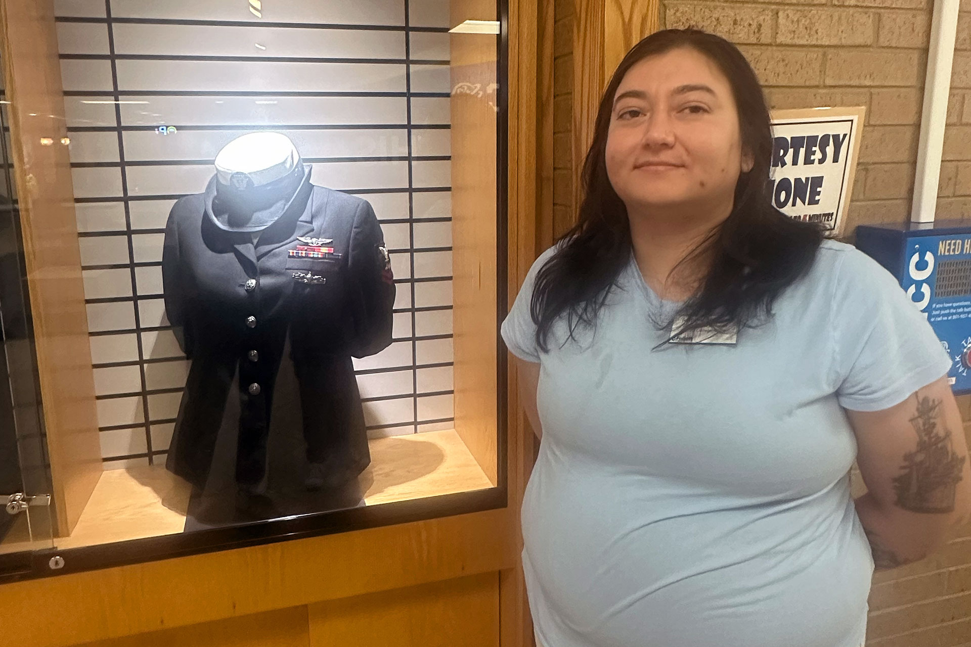 Avelina standing beside her Navy uniform being displayed in a shadowbox