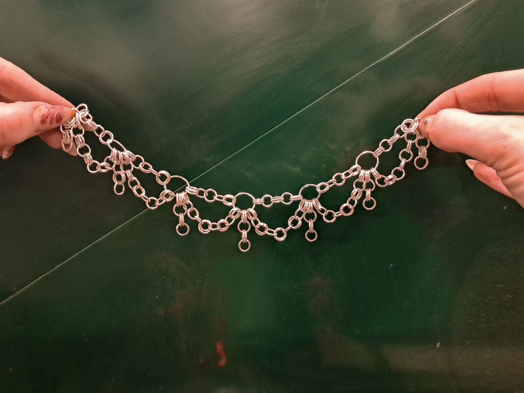 Woman's hands holding a necklace in front of a green background