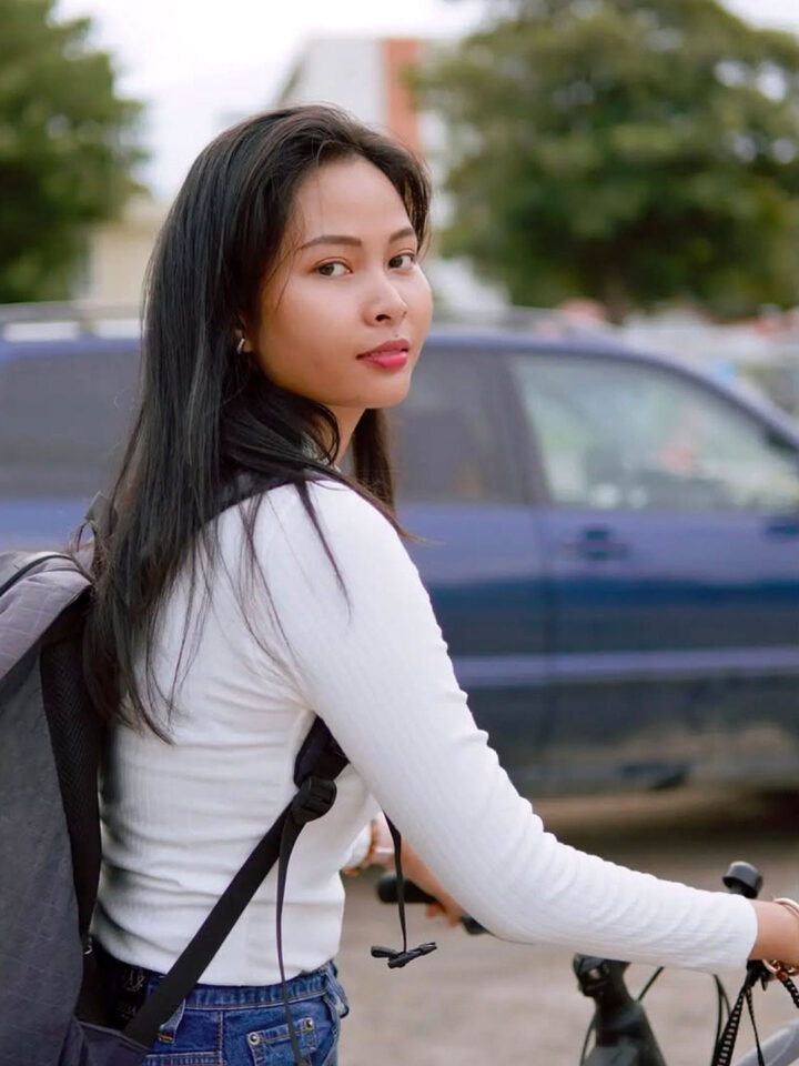 Chan Phall wearing a backpack and holding the handles of a bicycle