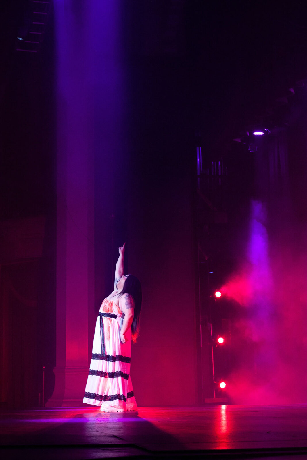 Agony Raye pointing upward while singing on stage