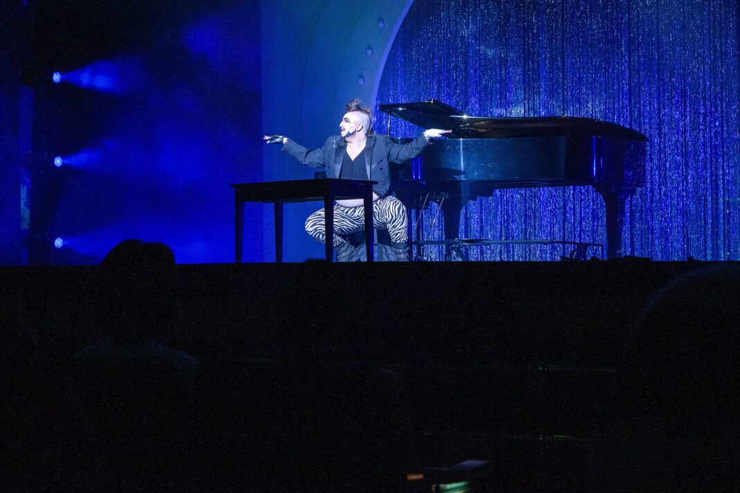 Notta Genda on stage singing next to a piano