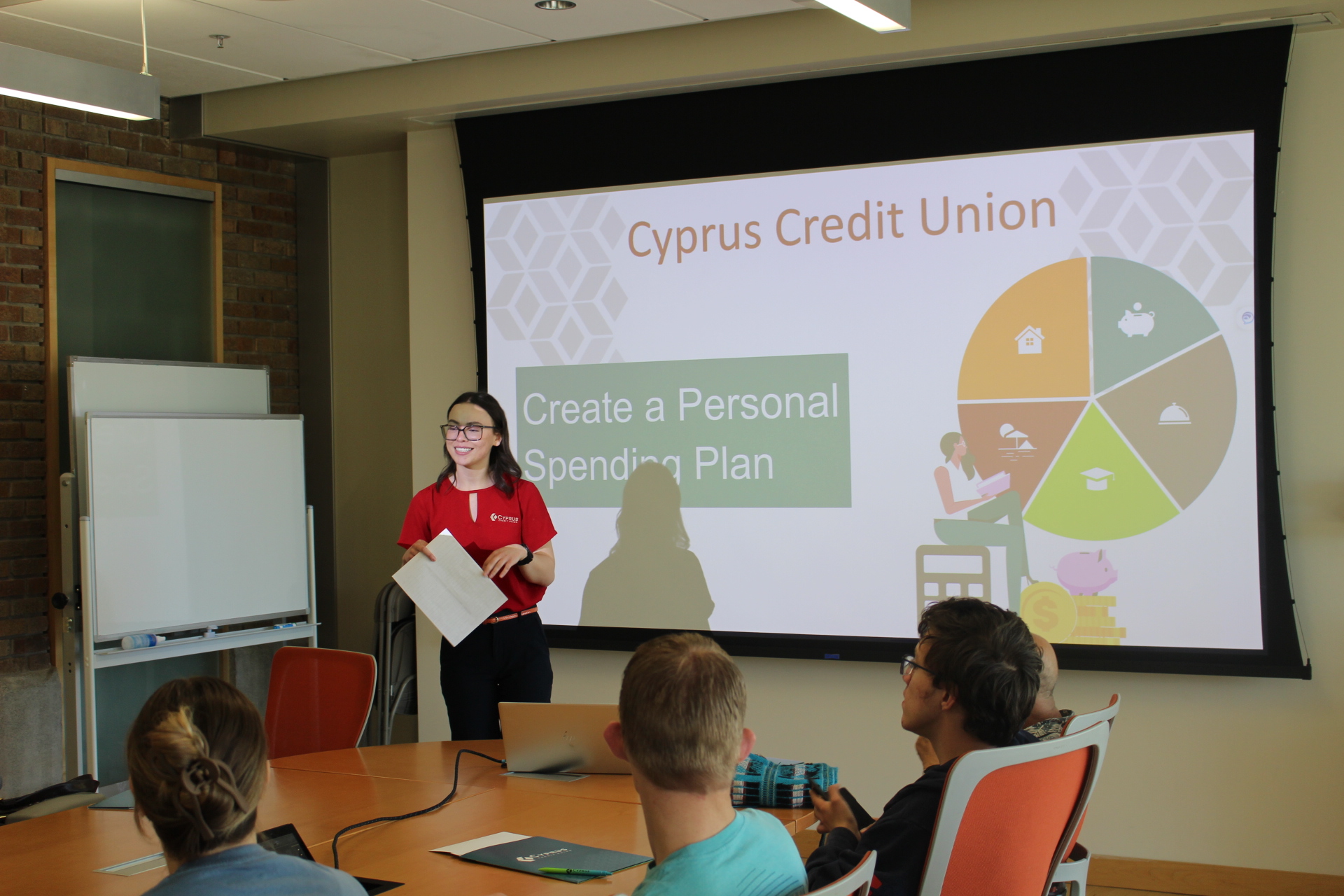 Luci explaining a personal spending plan during a presentation to students