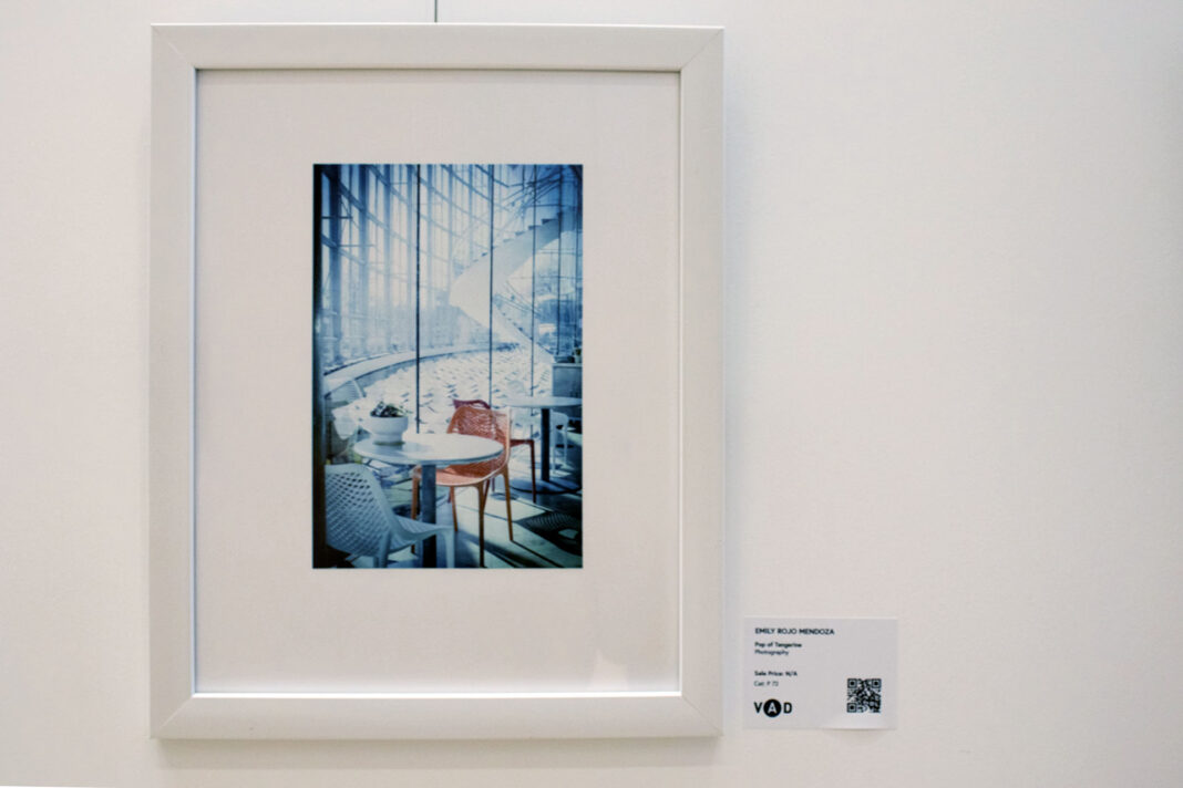Framed photograph of a tangerine colored chair sitting in a predominantly white building