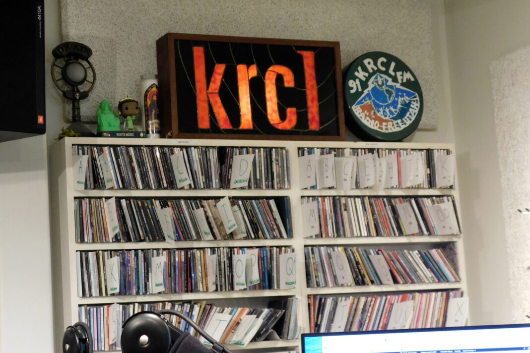 KRCL sign lit up atop a shelf of CDs