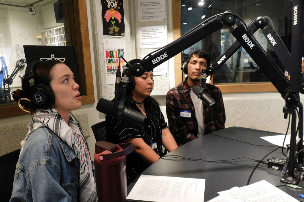 Three students sitting at microphones during a radio show