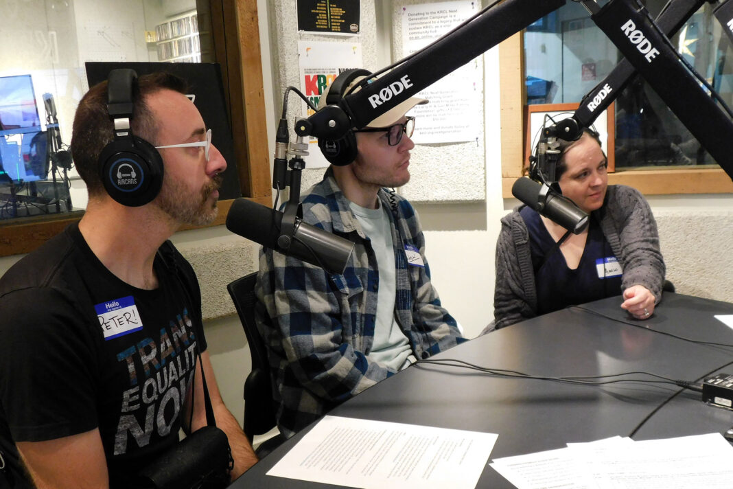 Three people sitting behind microphones at a table during a radio show