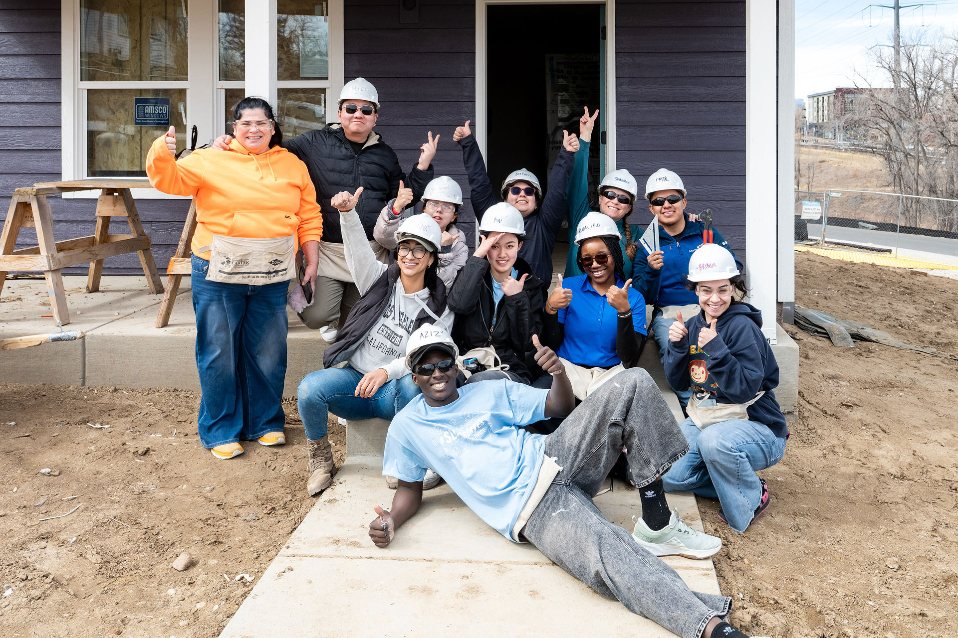 Students smiling and posing for a picture in front of a house under construction