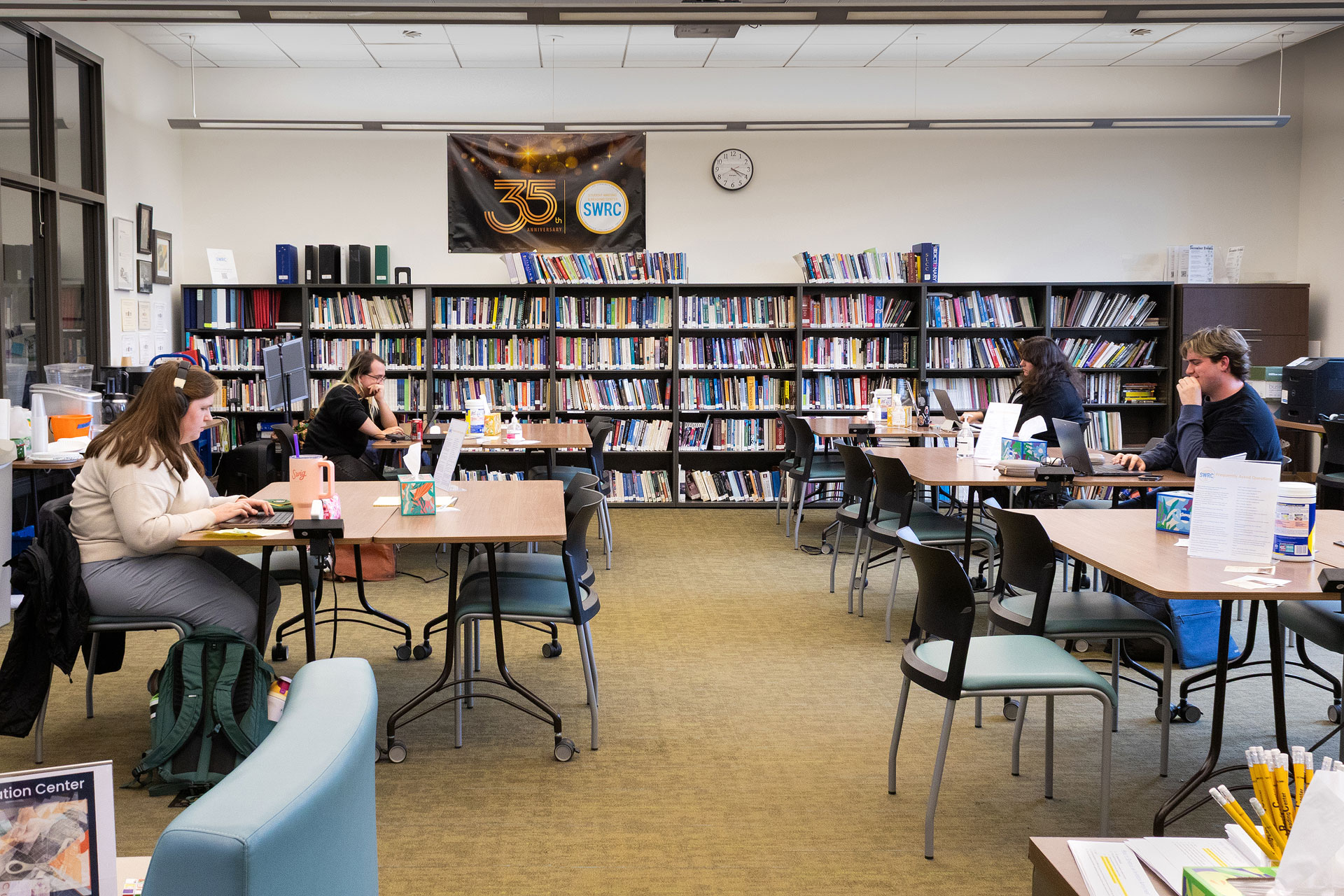 People sitting at desks inside a study room with a wall of books on shelves