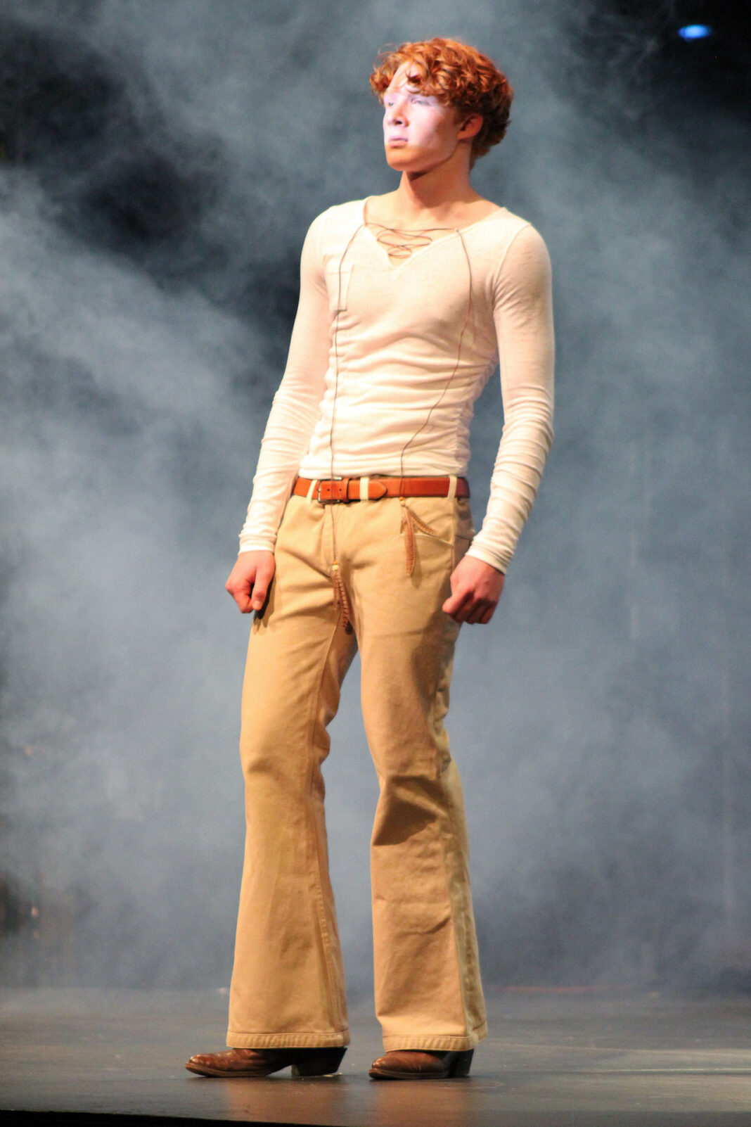 Model wearing a white shirt and beige pants on a stage