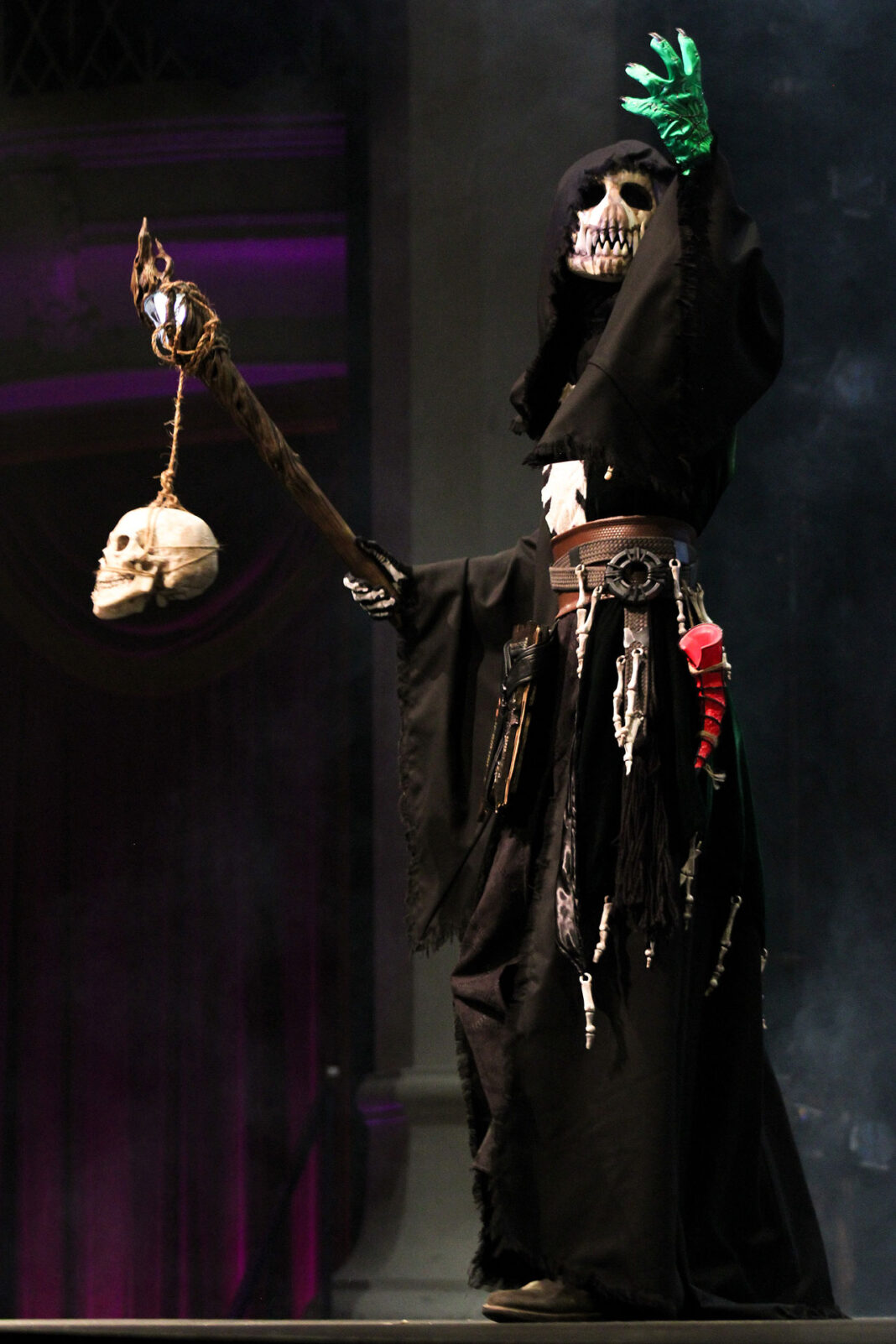 Model wearing a skull mask underneath a black cloak with weapons made of skull and bones