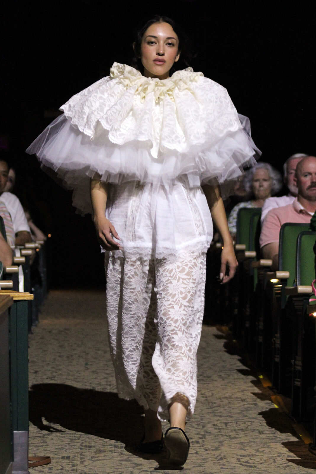 Model walking down an aisle wearing a white patterned outfit