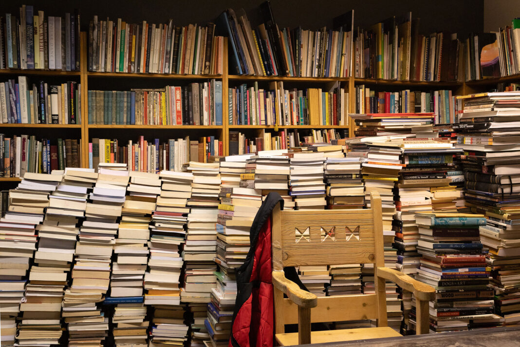 Hundreds of books stacked in piles on a floor in front of full bookshelves