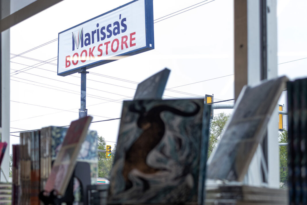 Books on display blurred in foreground with focus on large outdoor sign for Marissa's Bookstore