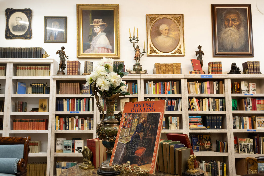 Framed portraits hanging on a wall above full bookshelves