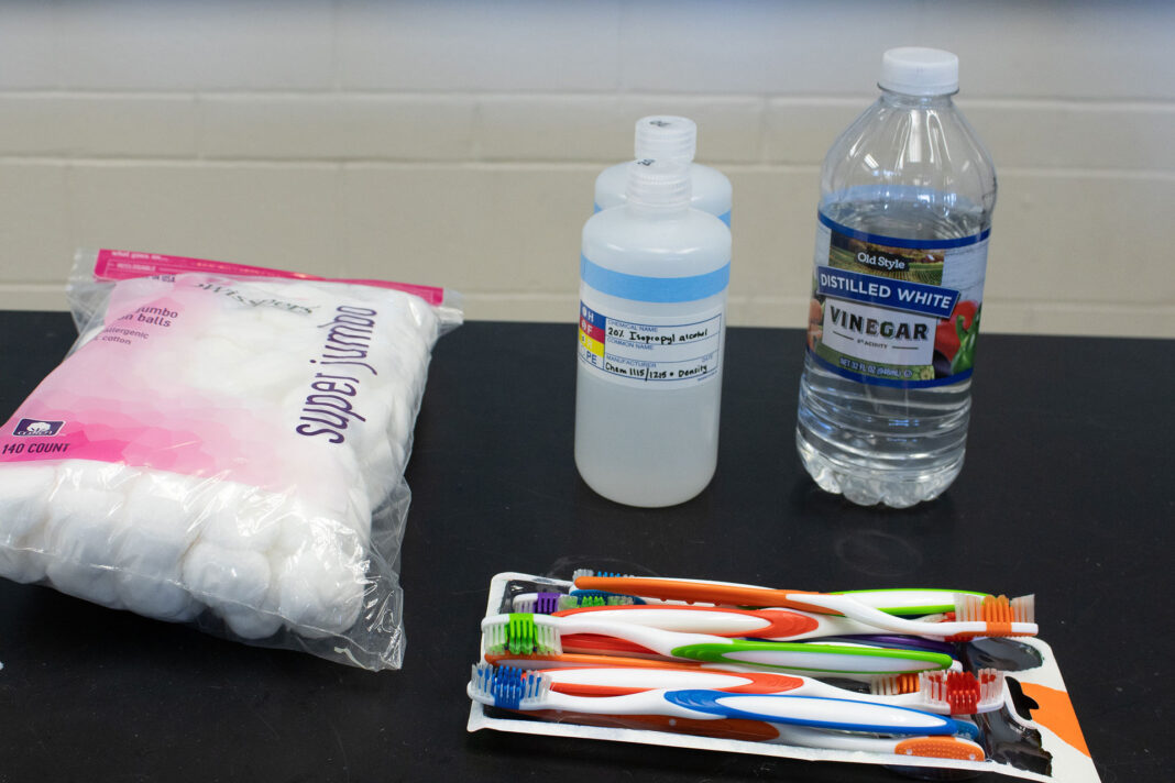 A package of cotton balls, toothbrushes, a bottle of vinegar and two bottles of isopropyl alcohol sitting on a table