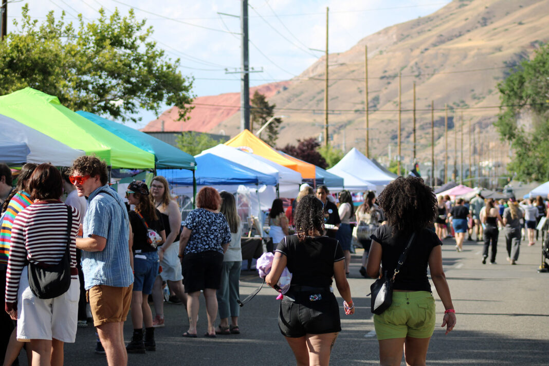 Festivalgoers socializing and walking past vendor booths on a city street