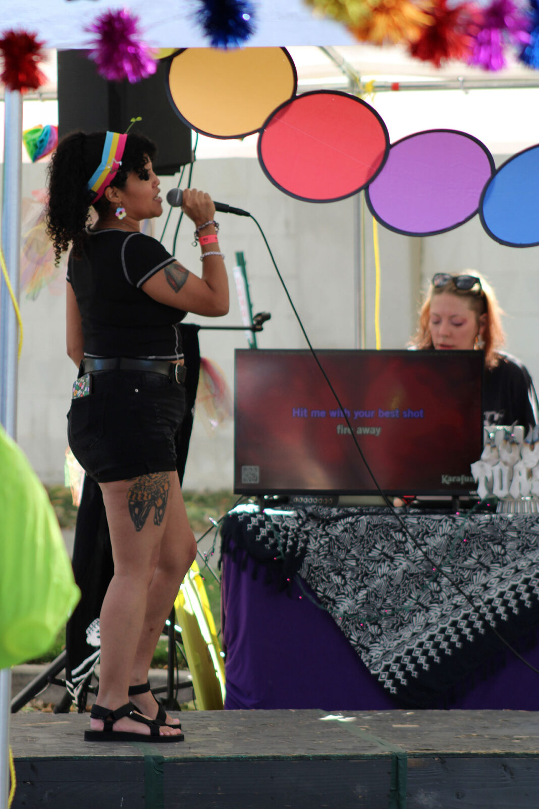 Woman singing on stage with "Hit Me With Your Best Shot" lyrics on a TV screen