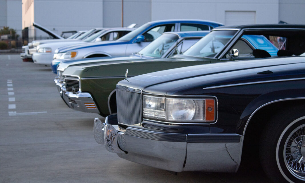 Cars of different eras and styles being displayed in a row during an outdoor event