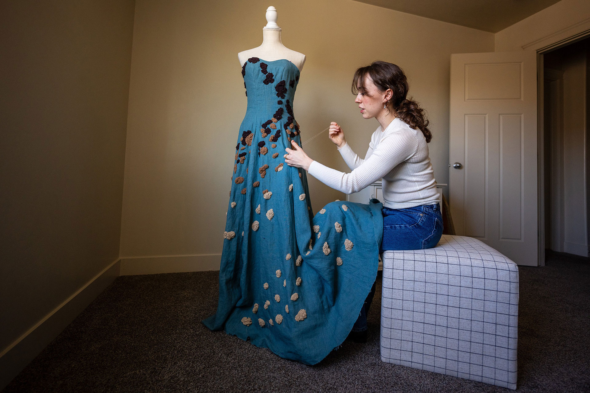 Ysabel working on her dress design while seated on an ottoman