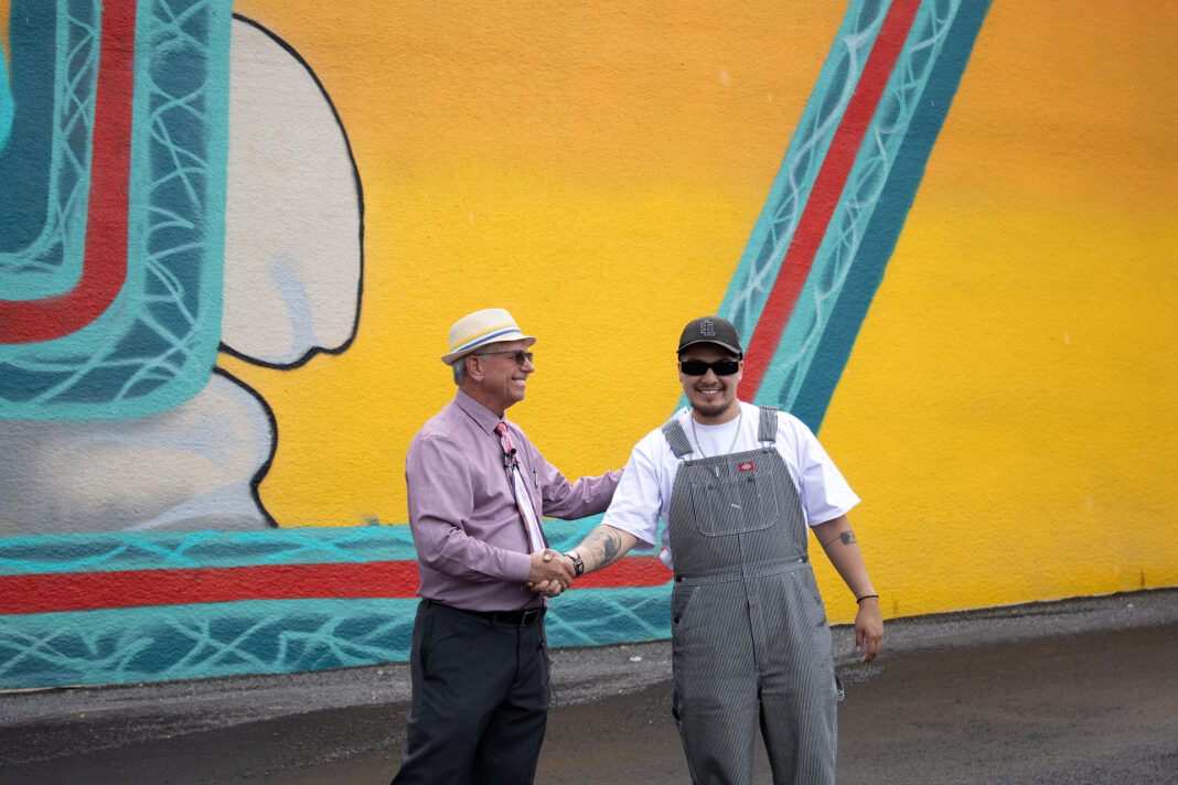 Dirk Burton and Beto Conejo smiling and shaking hands in front of Conejo's mural