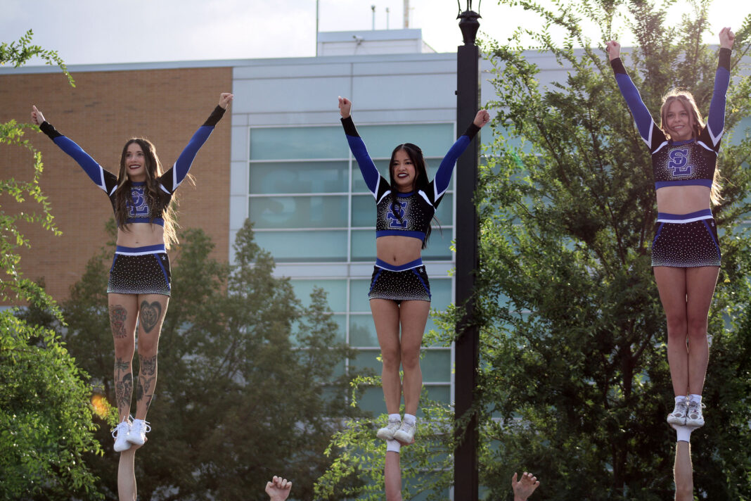 Three female cheerleaders balancing on male cheerleaders' hands