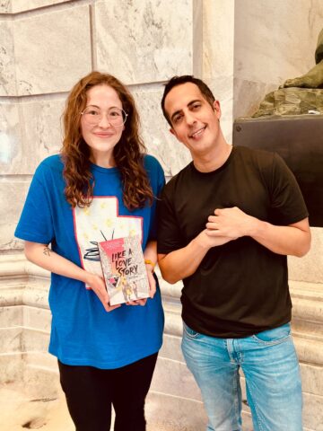 Cass and Abdi standing together while Cass holds his book