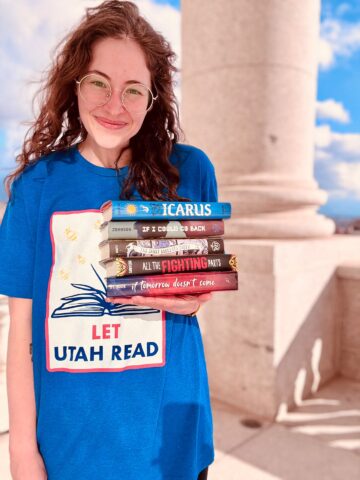 Cass wearing a t-shirt that says "Let Utah Read" while holding a stack of books