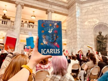Hand holding up "Icarus" in foreground, as group of people sitting in chairs hold up other books