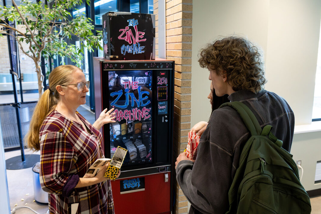 Landscape style photo of Brenda Sieczkowski explaining to students how the Zine Machine works