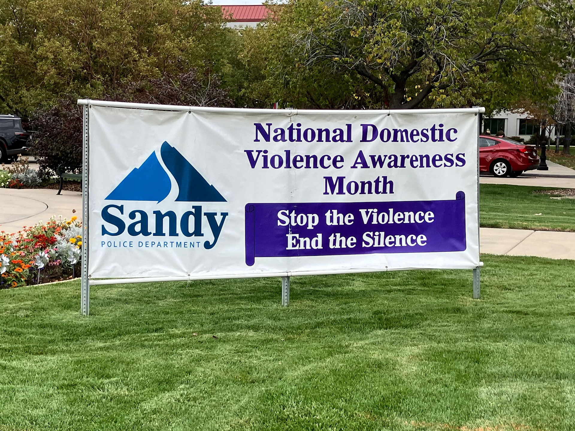 Large banner on a Sandy City lawn announcing National Domestic Violence Awareness Month - "Stop the Violence, End the Silence"