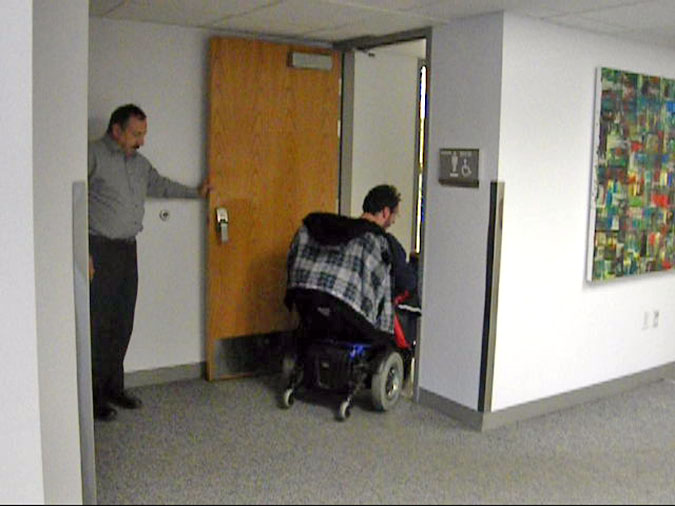 Facilities Services responsive to complaints Russ Collett assists Anthony Nelson enter the restroom at Meadowbrook Campus. Facilities Services is currently searching for a solution to have the door electronically activated.