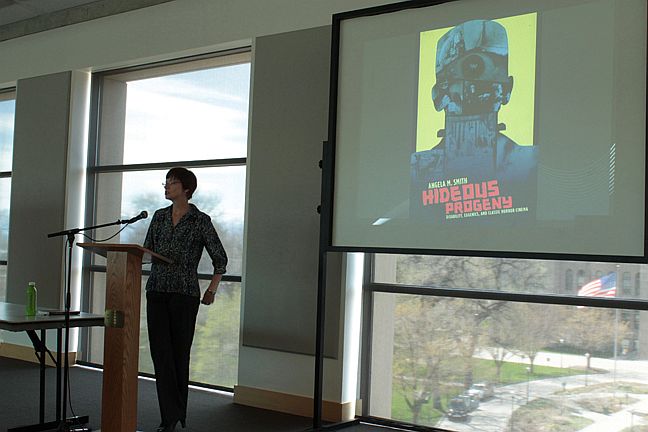 Lecture on horror cinema explores disability and eugenics Angela Smith at the podium opening her presentation with the cover of her book on the projection screen.